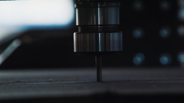 Timelapse of CNC head, Minimal frontal close up of a CNC bit suspended just above a flat board surface.