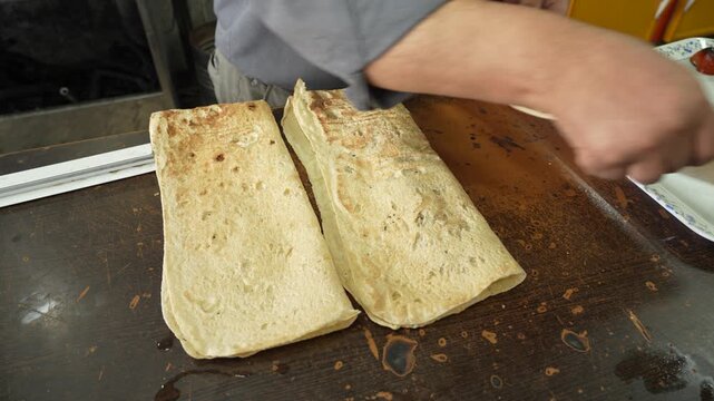 A cook places a meat kebab in an Arabic flatbread