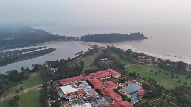 A drone shot capturing a sprawling seaside resort in Goa Patnem Beach, less crowded, surrounded by lush greenery, coastal backwaters, and a serene shoreline glowing beneath warm evening light.