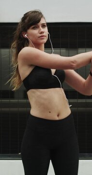 Fitness, earphones and stretching with woman in city for streaming service, health podcast and cardio. Wellness, exercise playlist and training music with person outdoor for runner, warm up and radio