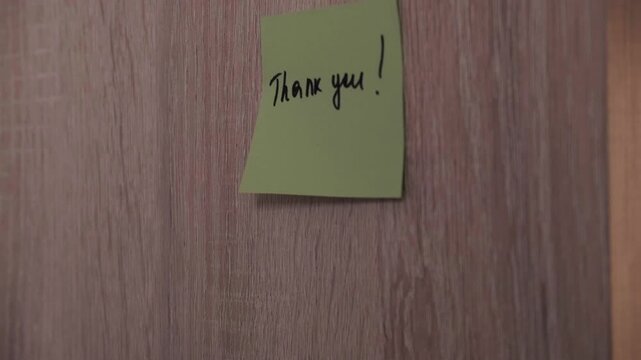 Hands stick a sticker with the text Thank you on a wooden surface. Video footage of courtesy and appreciation.