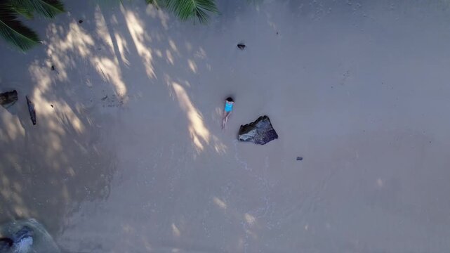 Vertical drone rocket shot revealing a woman relaxing on the white sands of Sunset Beach, Seychelles, surrounded by turquoise water and lush palms 30fps 002