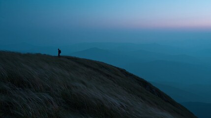 Obraz premium Lone hiker silhouetted on grassy ridge at dusk, overlooking layered mountain ranges under a serene twilight sky