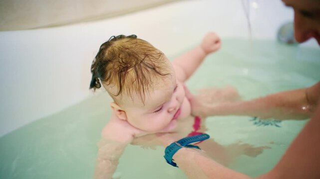 Baby enjoying bath time while being supported by a caregiver