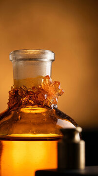 Extreme macro detail of large orange dichromate crystals formed around an amber bottle neck. The shallow depth of field emphasizes the complex mineral geometry and prestigious material quality.