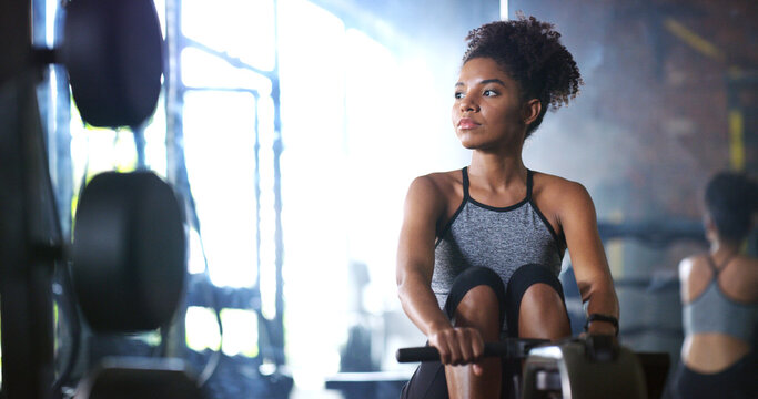 Woman, fitness and rowing machine in gym with exercise, endurance and strength training for wellness. Active, African person and workout in health club with ergometer, equipment and cardio challenge.