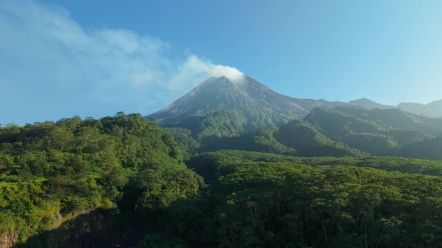Aerial view of Kali Gendol River and Mount Merapi volcano with smoke rising from the crater above lush green forests near Bunker Kaliadem in Pakem, Yogyakarta, Indonesia.