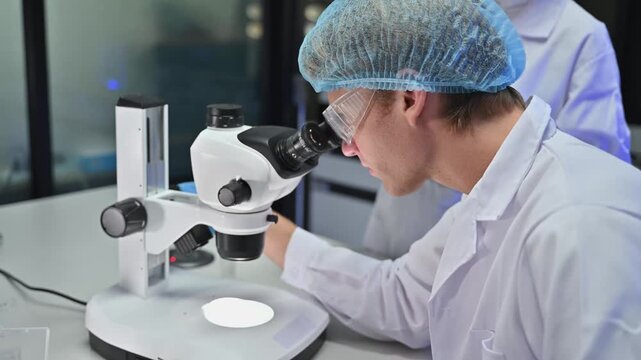 Professional Male Scientist Wear Goggles Examine Sample Through Microscope In Lab