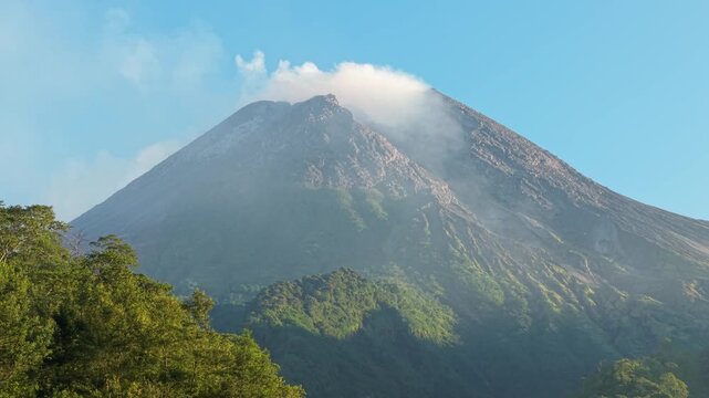 Aerial view of Mount Merapi with its smoking crater rising above lush green forests and the Bunker Kaliadem area in Kecamatan Pakem, Daerah Istimewa Yogya, Indonesia.