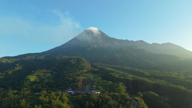 Aerial view of Bunker Kaliadem Merapi at the foot of Mount Merapi volcano surrounded by lush green forests under a clear blue sky in Kecamatan Pakem, Daerah Istimewa Yogya, Indonesia.