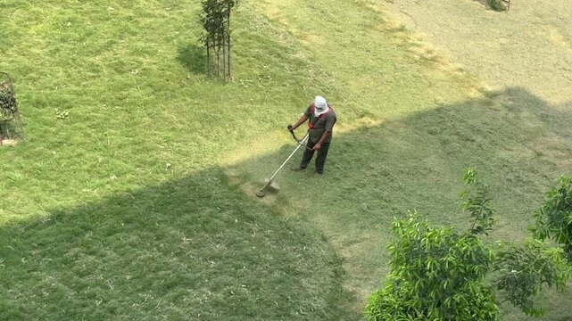 A Shot of Ground worker cutting grass with brush cutter machine in park