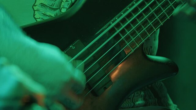 Close up shot of bassist's hand playing strings of black electric bass. Warm, intense lighting on musician at heavy metal concert or rehearsal. Dynamic composition