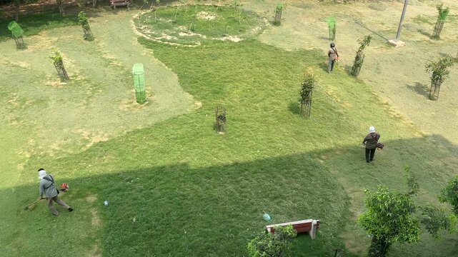 A Shot of Ground workers cutting grass with brush cutter machine in park
