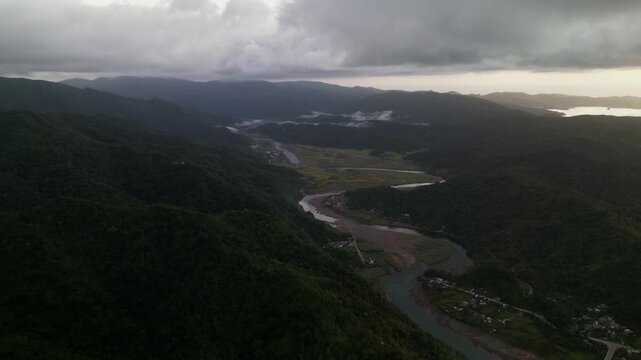 Panoramic aerial flyover of San Miguel, Catanduanes with winding river, mountain terrain, low clouds, and tropical valley landscape - Philippines