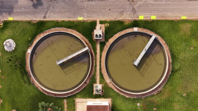 Overhead view of two secondary circular clarifiers at an urban wastewater treatment plant surrounded by green grass and adjacent road