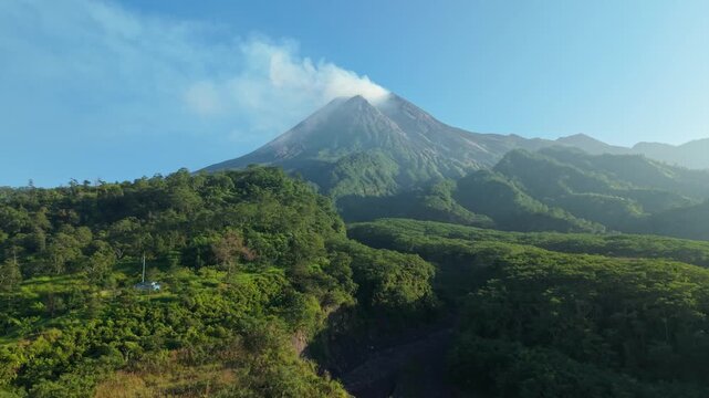 Aerial view of Bunker Kaliadem Merapi and the smoking peak of Mount Merapi with lush tropical forests and green hills in Kecamatan Pakem, Daerah Istimewa Yogya, Indonesia.