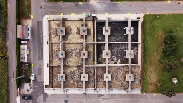 Top-down view of urban wastewater treatment plant bioreactor tanks with activated sludge, showing aeration basins with turbulent brown and dark water
