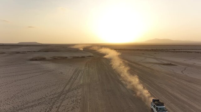 Aerial view of a vehicle driving across the arid landscape of the Danakil Desert, leaving a trail of dust under the golden sunset light in Dalol, Afar, Ethiopia.
