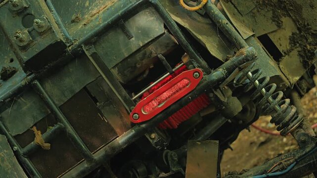 A detailed view of the dirty chassis of an all-terrain vehicle. The winch winds a bright red cable. The concept is extreme sports, off-roading, power, and adventure