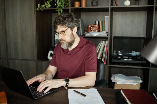 Middle aged Caucasian man typing on laptop at desk, while working on new novel at home 