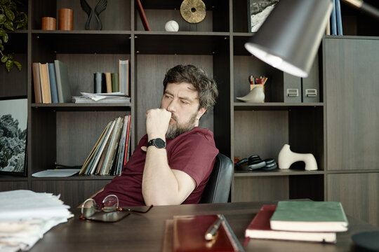 Caucasian middle aged man sitting at desk, thinking through problem in home office, representing decision making and work stress
