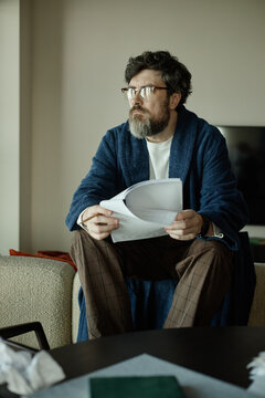 Vertical shot of middle aged Caucasian man reviewing chapter of brand new novel and holding pencil at home
