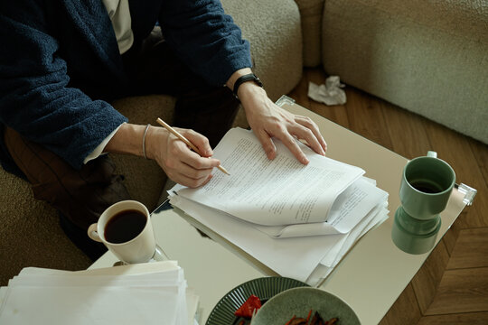 Overhead shot of middle aged adult reviewing printed chapters of novel, taking personal notes and coming up with plot twists
