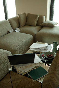 Vertical shot of home office corner showing laptop, paperwork, notebook, tissues, coffee cup, sofa. Illustrating remote work overload, burnout, productivity stress, work life balance content
