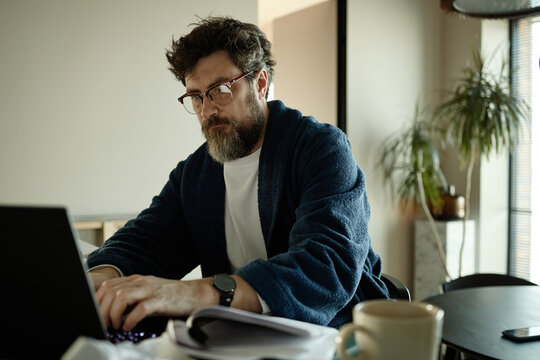Middle aged Caucasian man working on laptop at home, typing and reviewing chapters 