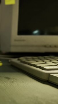 A keyboard rests on a wooden desk while a computer monitor sits nearby. The setting is a simple tech workspace. Light reflects off the screen at an angle.