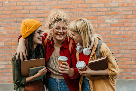 Three happy female students laughing enjoying coffee break
