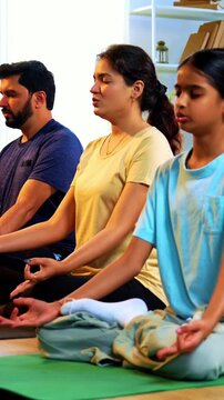 Indian young family doing omkar meditation pranayama at home chanting aum breathing yoga together indoors during peaceful morning hours in a modern living room promoting yogic lifestyle