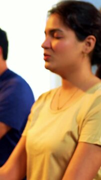 Indian young family doing omkar meditation pranayama at home chanting aum breathing yoga together indoors during peaceful morning hours in a modern living room promoting yogic lifestyle