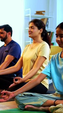 Indian young family doing omkar meditation pranayama at home chanting aum breathing yoga together indoors during peaceful morning hours in a modern living room promoting yogic lifestyle