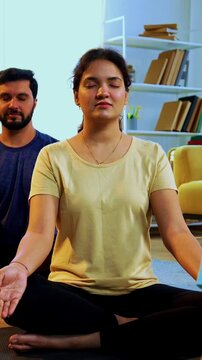 Indian young family doing omkar meditation pranayama at home chanting aum breathing yoga together indoors during peaceful morning hours in a modern living room promoting yogic lifestyle