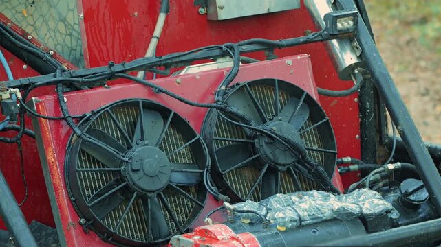 Detail shot of custom off road buggy. Focus on dual black cooling fans on red radiator. Wet and dirty components suggest intense racing. Industrial and powerful concept for motorsports