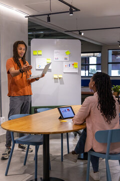 Team presenting at work board man orange tee using laptop woman pink blazer tablet, copy space