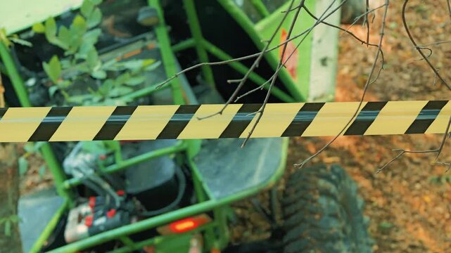 High angle view of green all terrain buggy at outdoor event. Yellow and black warning tape in foreground with tree branches, creating restricted area concept for extreme sports competition