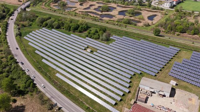 Aerial view of a large solar panel farm situated next to a road with cars and industrial buildings in Slavkov u Brna, South Moravian Region, Czechia.