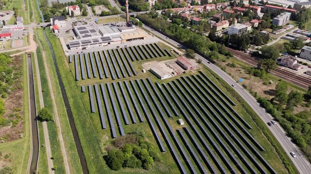 Aerial view of a solar farm and industrial facility with photovoltaic panels and a tall chimney near residential areas in Slavkov u Brna, South Moravian Region, Czechia.