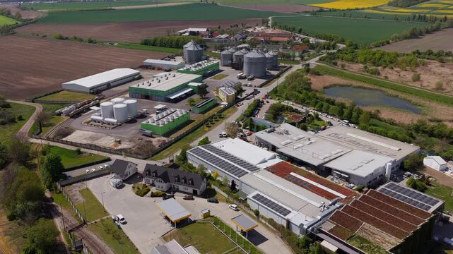 Aerial view of an industrial complex with storage silos and warehouses surrounded by green fields in Slavkov u Brna, South Moravian Region, Czechia.