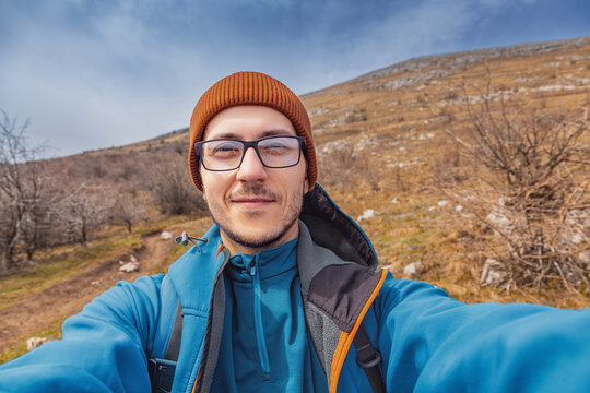 Hiker enjoying personal achievement and freedom at mountain summit, smiling at camera with a rugged landscape