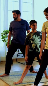 Indian family doing virabhadrasana yoga at home practicing warrior pose together indoors for healthy body and calm mind during morning routine inside a modern lavish living space 