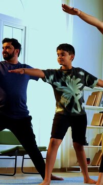 Indian family doing virabhadrasana yoga at home practicing warrior pose together indoors for healthy body and calm mind during morning routine inside a modern lavish living space