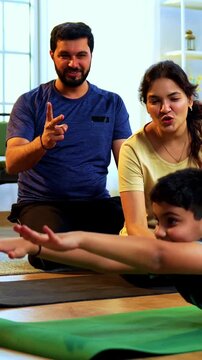 Indian kid doing boat pose yoga or naukasana exercise at home practicing core balance on floor while family watches indoors during calm morning hours in a modern lavish living space promoting health