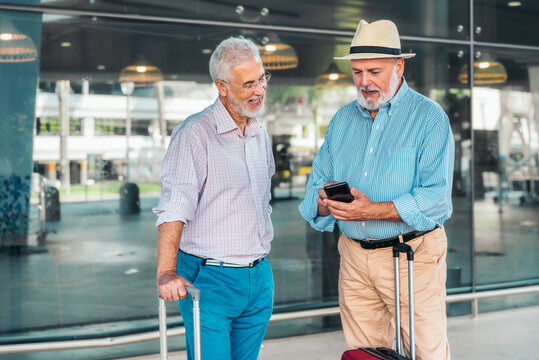 Two senior men checking travel plans while looking at a smartphone at the airport
