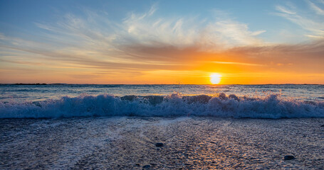 Obraz premium Dramatic Golden sunset over tranquil beach, waves lashing the pebble coastline