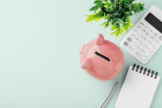 Pink piggy bank with calculator and spiral notebook on pastel green background, flatlay, finance planning, personal savings, and budgeting