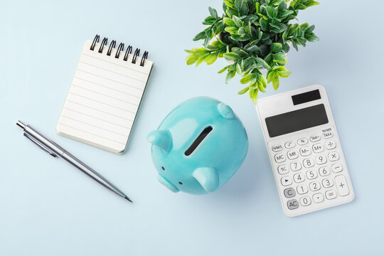 Piggy bank with calculator and blank notebook on light blue background, flatlay, personal finance tracking, accounting, tax planning, and budgeting