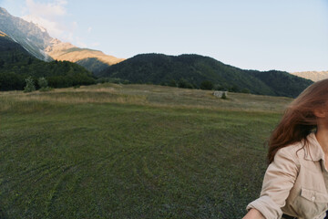 Fototapeta premium Woman lifestyle in an open field with distant mountains, natural landscape, casual beige jacket, feeling of freedom and outdoor exploration under a sunny sky